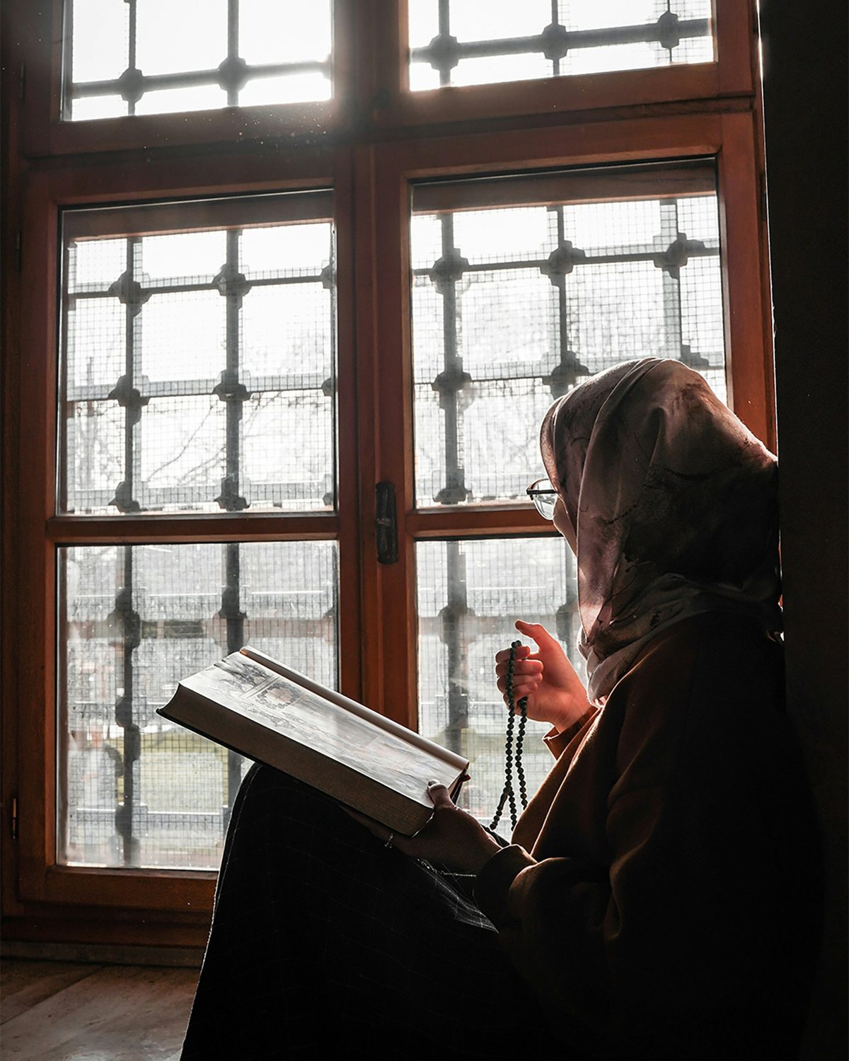 قارئة تقرأ كتابًا ورقيًا عند نافذة صباحًا